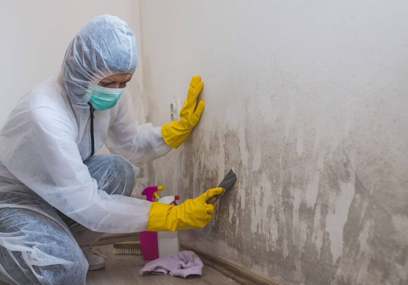 Person cleaning mold from wall in protective gear.